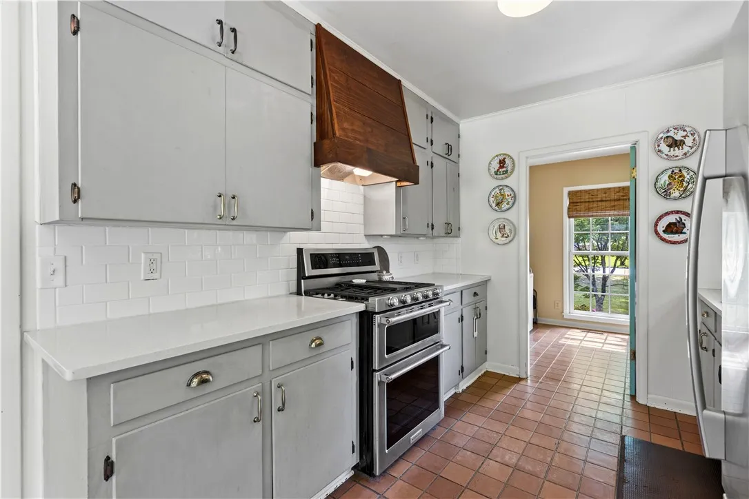 Terracotta tile floors pair with quartz countertops and a wood range hood in this kitchen.