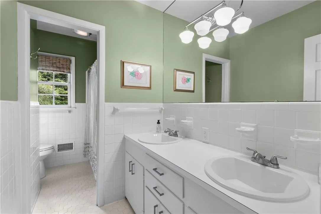 Classic white tile wainscoting pairs with a dual-sink vanity in this hall bathroom.