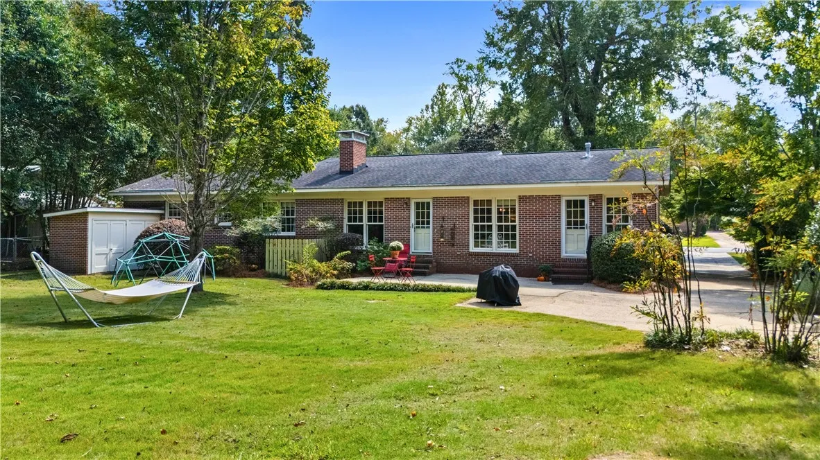 Mature trees frame a classic brick exterior opening to a grassy lawn.