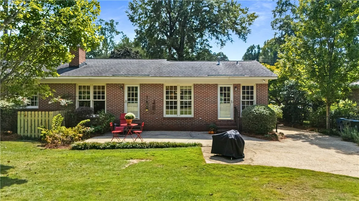 A spacious concrete patio stretches along the brick exterior, overlooking a mature green lawn.