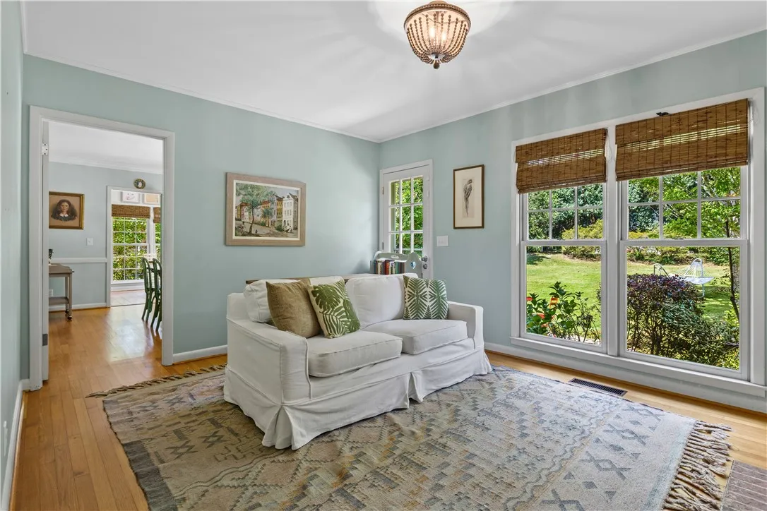 Polished hardwood floors and generous windows framing green backyard views enhance this welcoming den space.