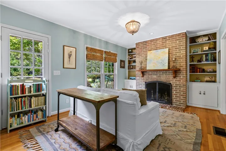 A classic brick fireplace anchors the den alongside warm hardwood flooring and built-in shelving.