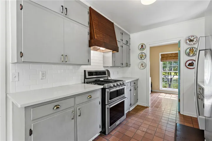 Terracotta tile floors pair with quartz countertops and a wood range hood in this kitchen.