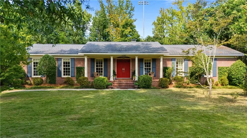 Classic brick exterior showcases a welcoming front porch framed by mature trees and lush green lawn.