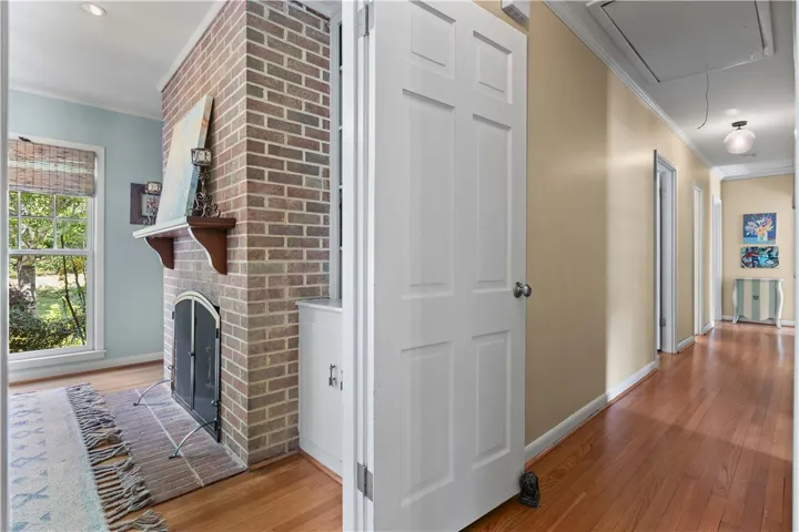 Rich hardwood flooring guides the eye past a classic brick fireplace and down a welcoming hallway.