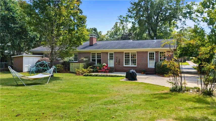 Mature trees frame a classic brick exterior opening to a grassy lawn.