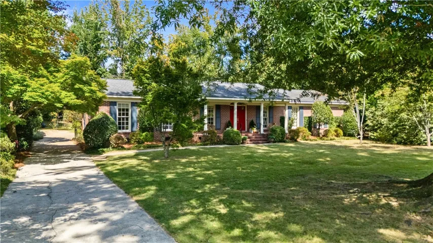 Mature trees frame a classic brick exterior with a welcoming front porch and concrete driveway.