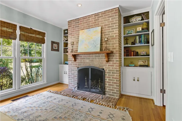 An inviting brick fireplace flanked by built-in shelving anchors this hardwood-floored den.