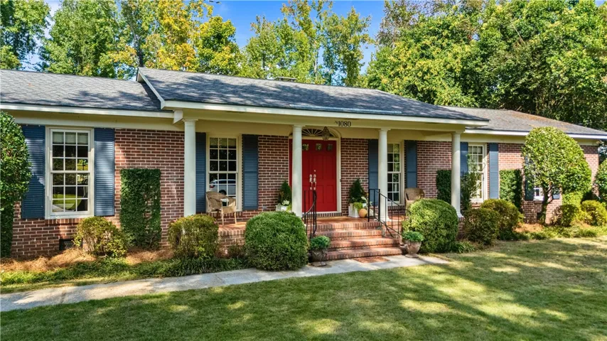A welcoming front porch with classic brick siding and a bright entry door greets visitors.
