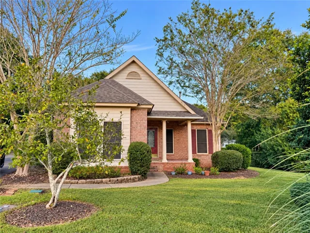 Mature trees and neat landscaping frame a classic brick home with an inviting front porch.