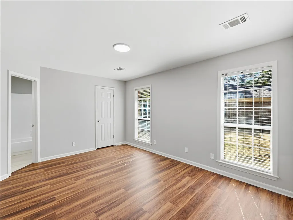 Warm wood-look flooring and generous windows define this versatile bedroom space.