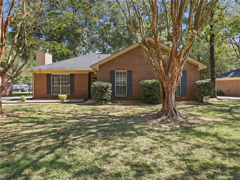 Mature trees shade a classic brick exterior featuring contrasting shutters and a gabled roofline.