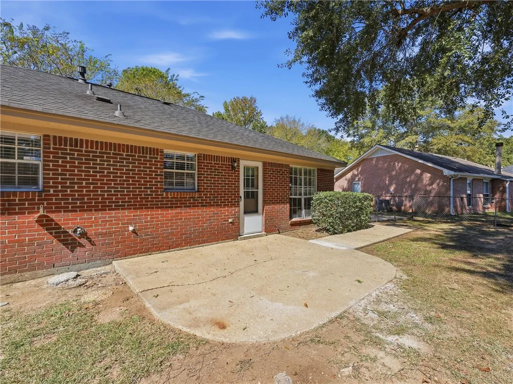 Classic brick architecture defines this rear exterior featuring a concrete patio under mature trees.