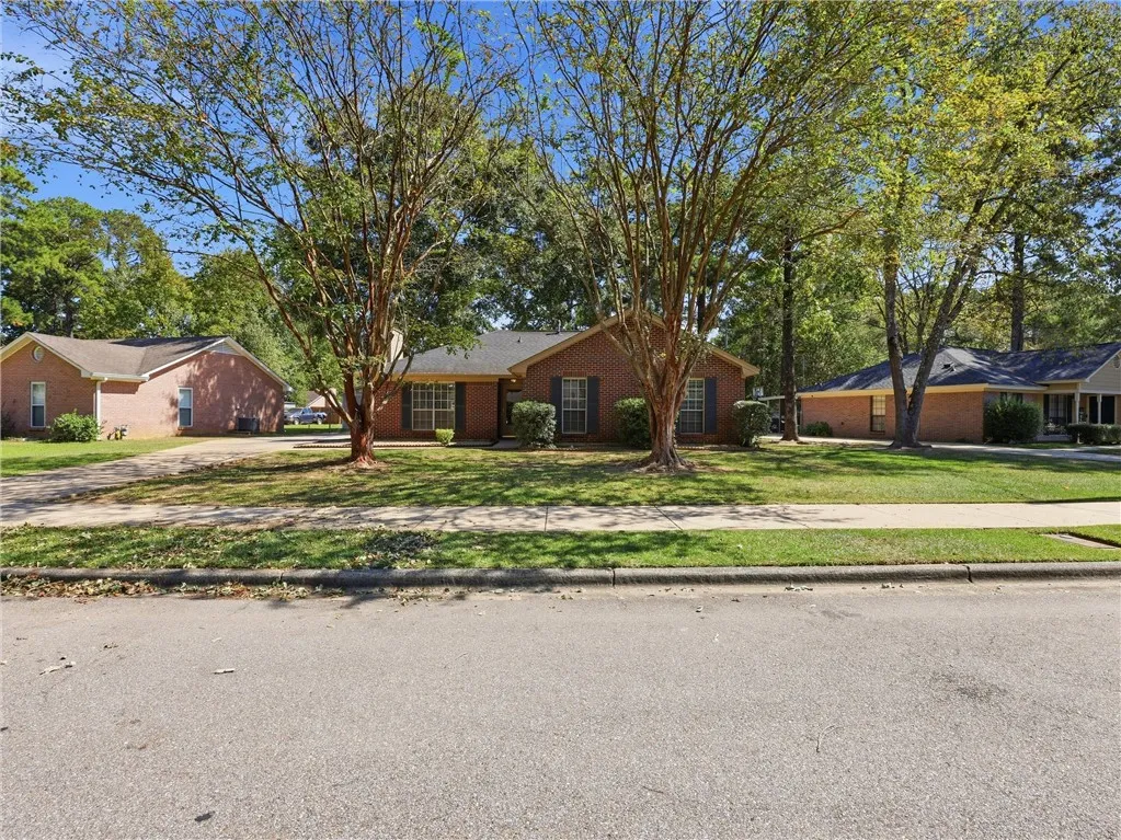 Mature trees frame the classic brick exterior of this inviting single-story home.