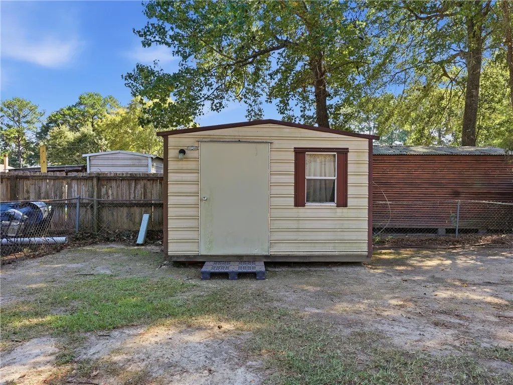 A practical storage shed sits within the fenced backyard surrounded by mature trees.