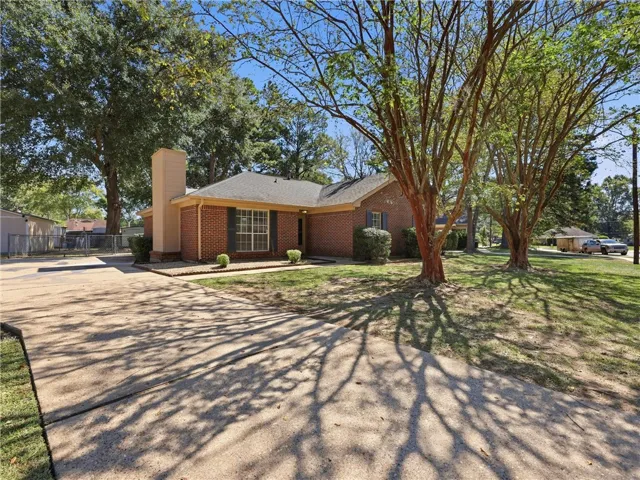 Mature trees shade a classic brick exterior and a wide concrete driveway.
