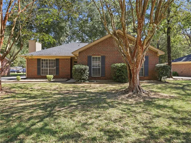 Mature trees shade a classic brick exterior featuring contrasting shutters and a gabled roofline.