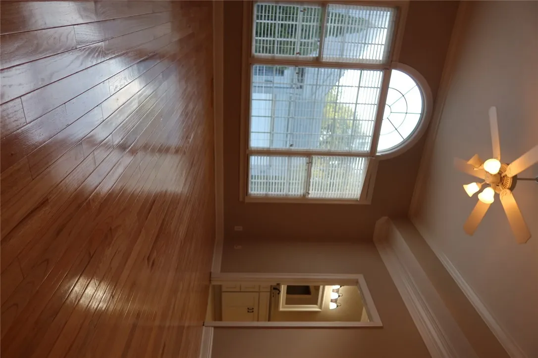 Gleaming hardwood floors reflect natural light from a classic arched window flanked by detailed crown molding.