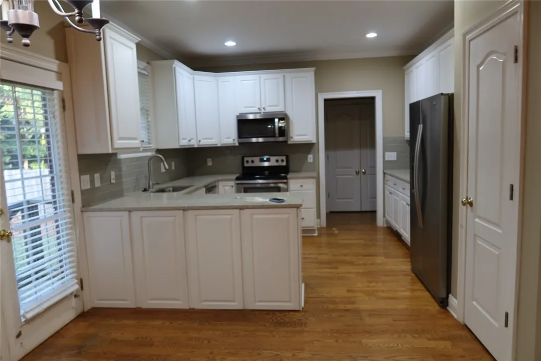 Rich hardwood floors anchor this timeless kitchen boasting stone countertops and white cabinetry.