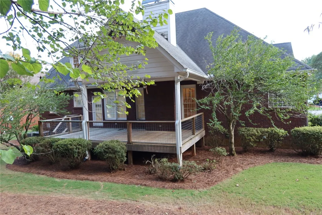 An elevated wooden deck extends from the brick exterior, overlooking a sloping lawn and mature trees.