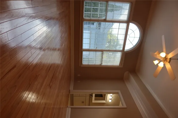 Gleaming hardwood floors reflect natural light from a classic arched window flanked by detailed crown molding.