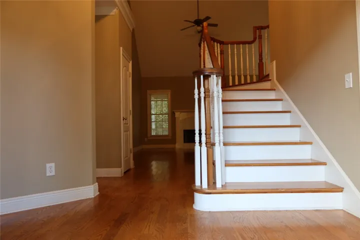 Rich hardwood floors lead past a graceful wooden staircase into the open living spaces.