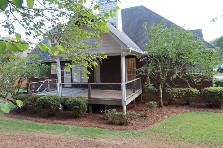 An elevated wooden deck extends from the brick exterior, overlooking a sloping lawn and mature trees.
