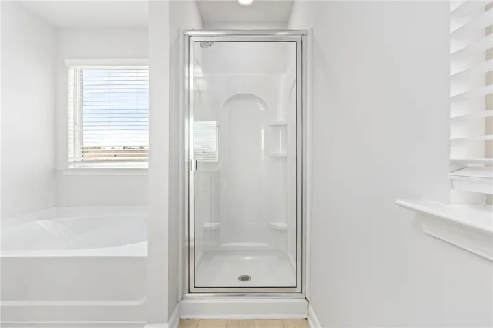 Natural light fills this space featuring a built-in tub and a separate glass-enclosed shower.