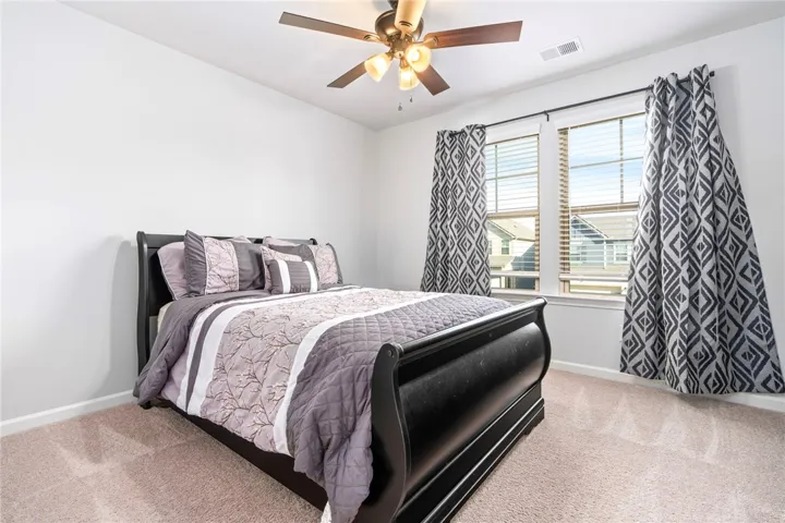 Double windows frame views of the neighborhood in this cozy bedroom with plush carpet flooring.