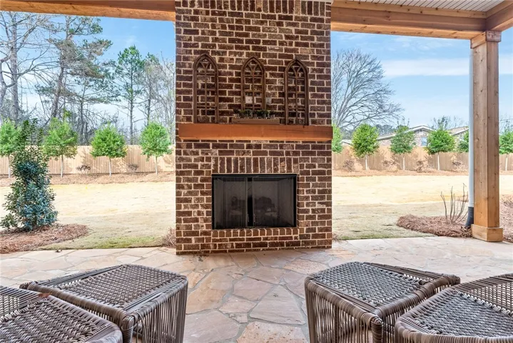 A robust brick fireplace anchors the covered stone patio overlooking a spacious backyard.