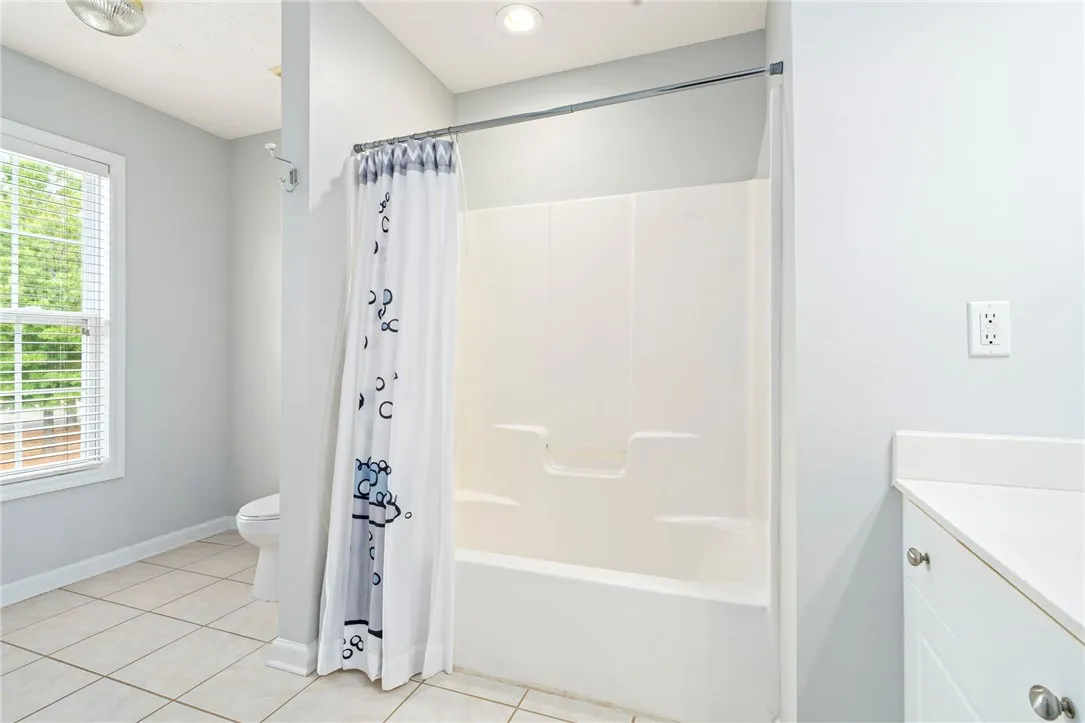 A light-filled bathroom features neutral tile flooring and a classic tub shower combination.