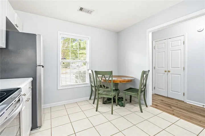 Sunlight streams through a large window into this cozy dining space with neutral tile flooring.