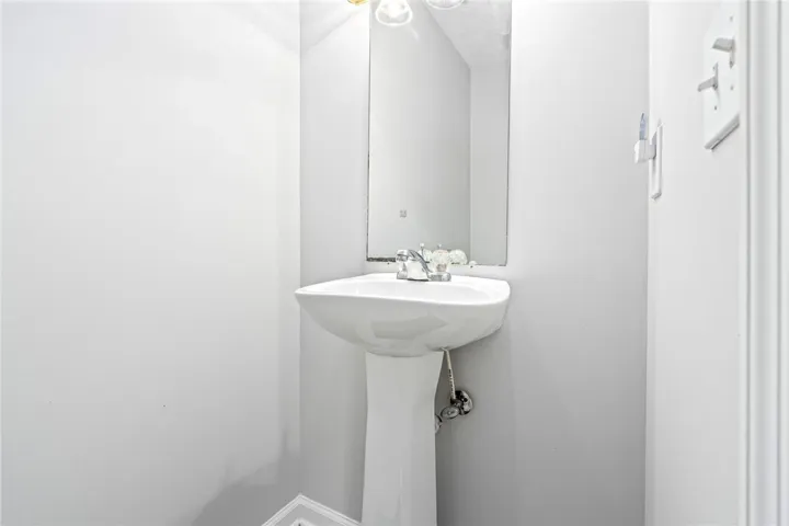 A classic pedestal sink sits beneath a simple wall-mounted mirror in this compact half bath.