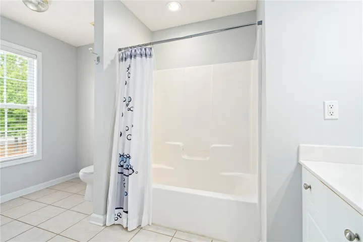 A light-filled bathroom features neutral tile flooring and a classic tub shower combination.