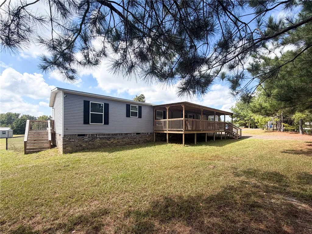 Mature trees frame a charming home featuring a spacious covered deck and a grassy yard.