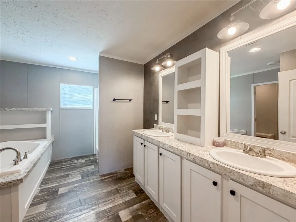 Wood-look flooring complements the spacious dual vanity and soaking tub in this refined bathroom layout.