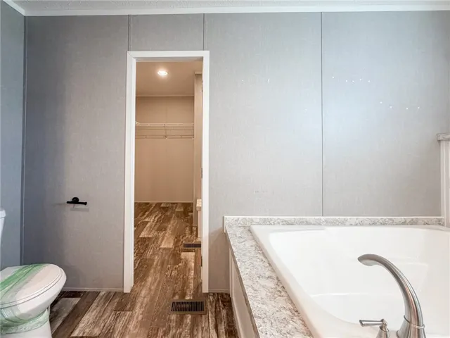 An inviting soaking tub pairs with wood-look flooring and a nearby walk-in closet.
