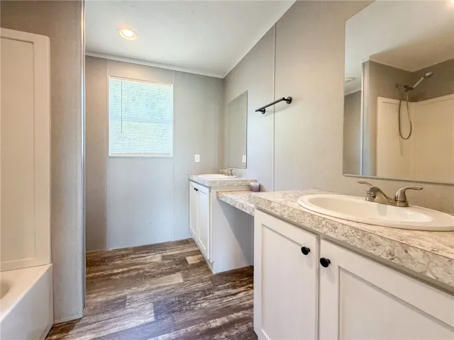 Rich wood-look flooring anchors this well-appointed bathroom featuring dual vanities and a crisp white​​‌​​​​‌​​‌‌​‌‌​​​‌‌​‌​‌​‌​​​‌​​ tub.
