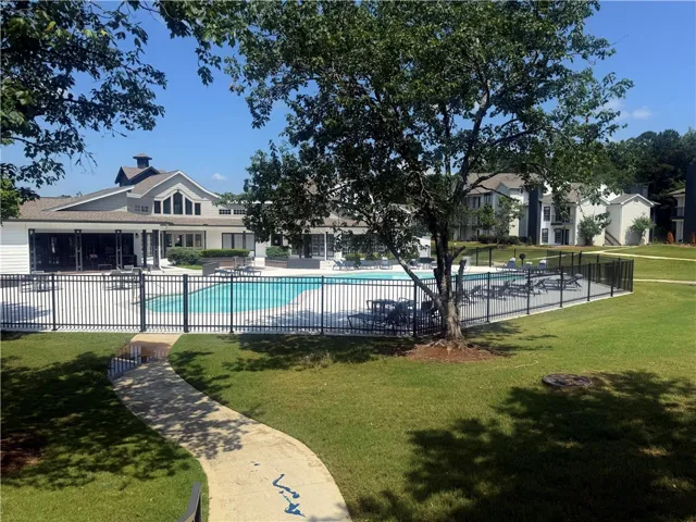 A fenced swimming pool sits adjacent to a clubhouse amid green lawns and mature trees.