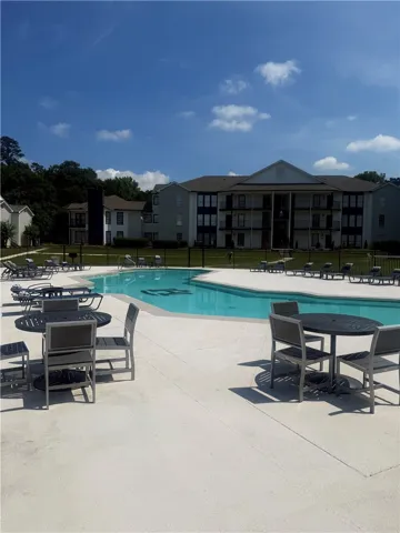 A sparkling community swimming pool rests beside multi-story residential buildings under clear blue skies.