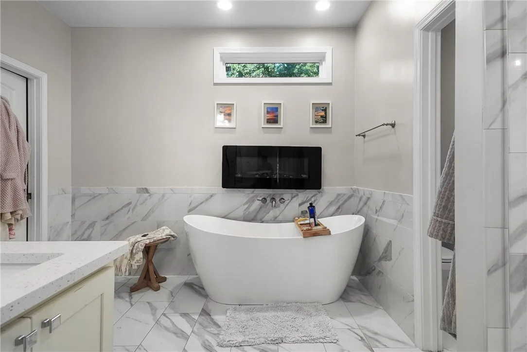 Elegant marble-style tiling surrounds a freestanding soaking tub in this light-filled modern bathroom.