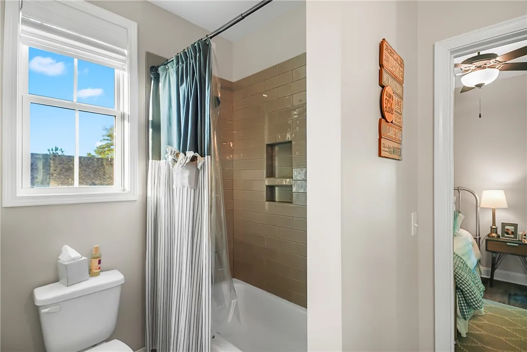 Glossy subway tile surrounds the shower and tub combination next to a bright window.
