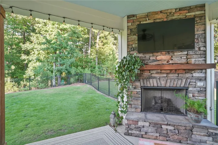 An inviting stone fireplace anchors this covered back porch overlooking a fenced grassy yard.