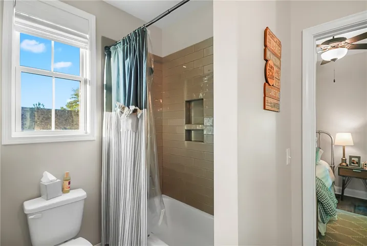 Glossy subway tile surrounds the shower and tub combination next to a bright window.