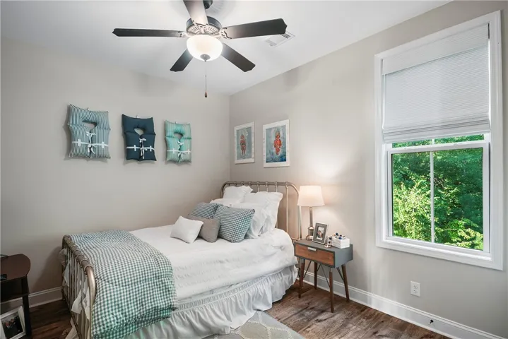 A bright bedroom showcases rich wood floors, high ceilings, and a tall window framing green views.