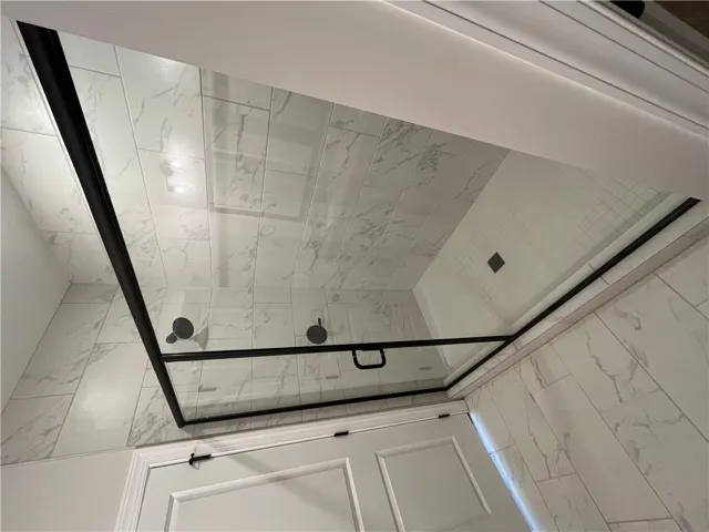 Floor-to-ceiling marble-patterned tile surrounds a modern glass shower enclosure with sleek black hardware.