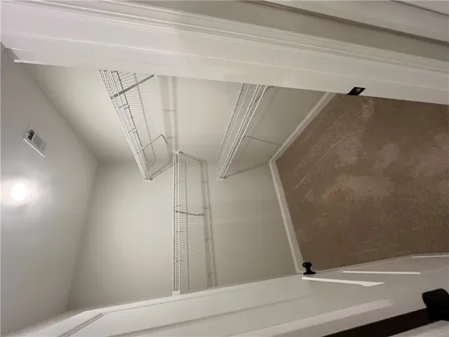 Ample wire shelving lines this functional walk-in closet featuring wall-to-wall carpeting.