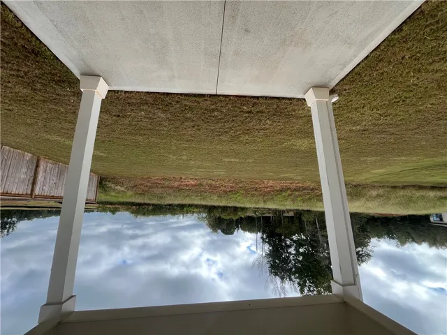 An open grassy backyard extends beyond a covered concrete patio supported by white columns.