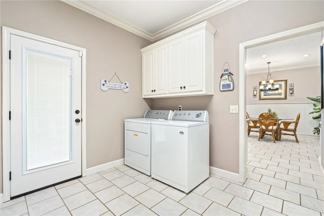 Functional laundry room features durable tile flooring, crown molding, and overhead storage cabinetry.