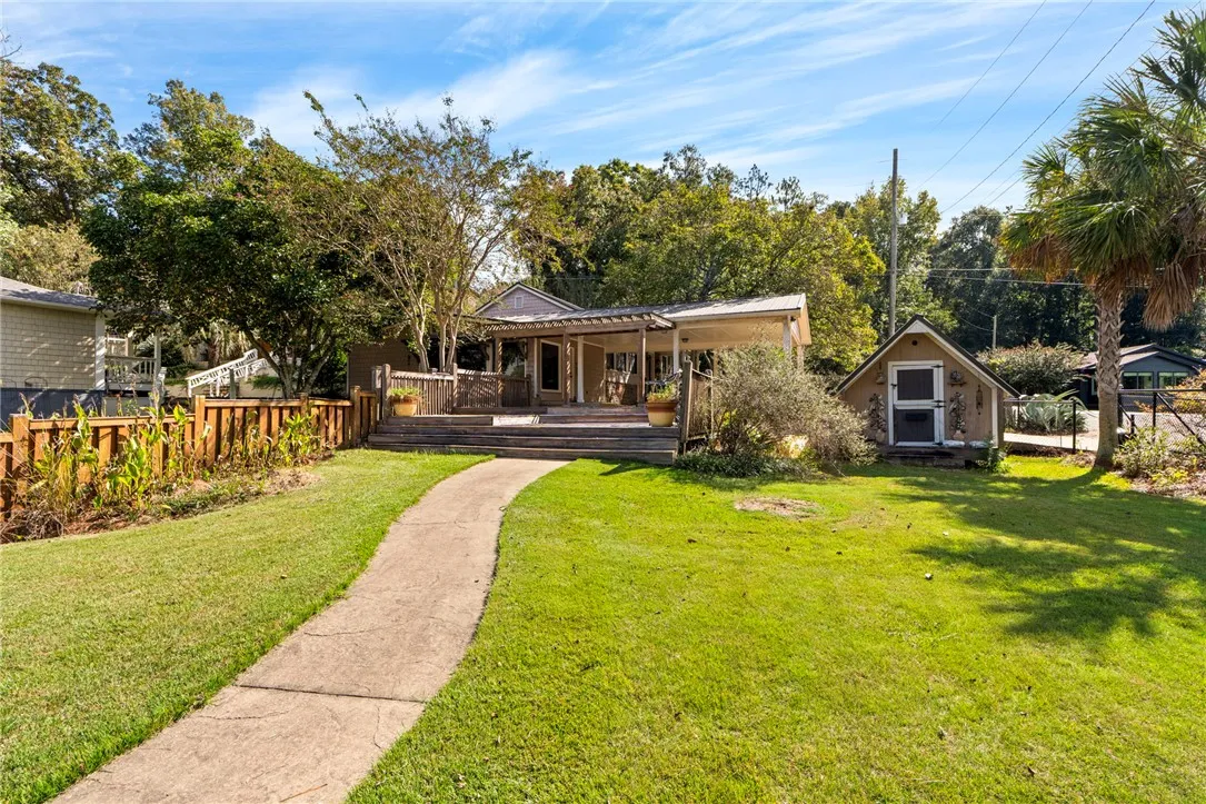 A concrete walkway leads through the grassy lawn toward the rear porch and detached shed.